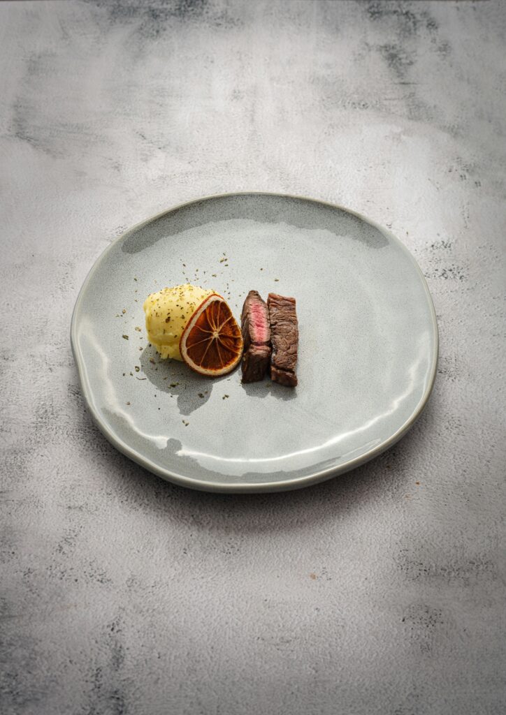 two tiny slices of steak with small scoop of mashed potato and a dried orange slice