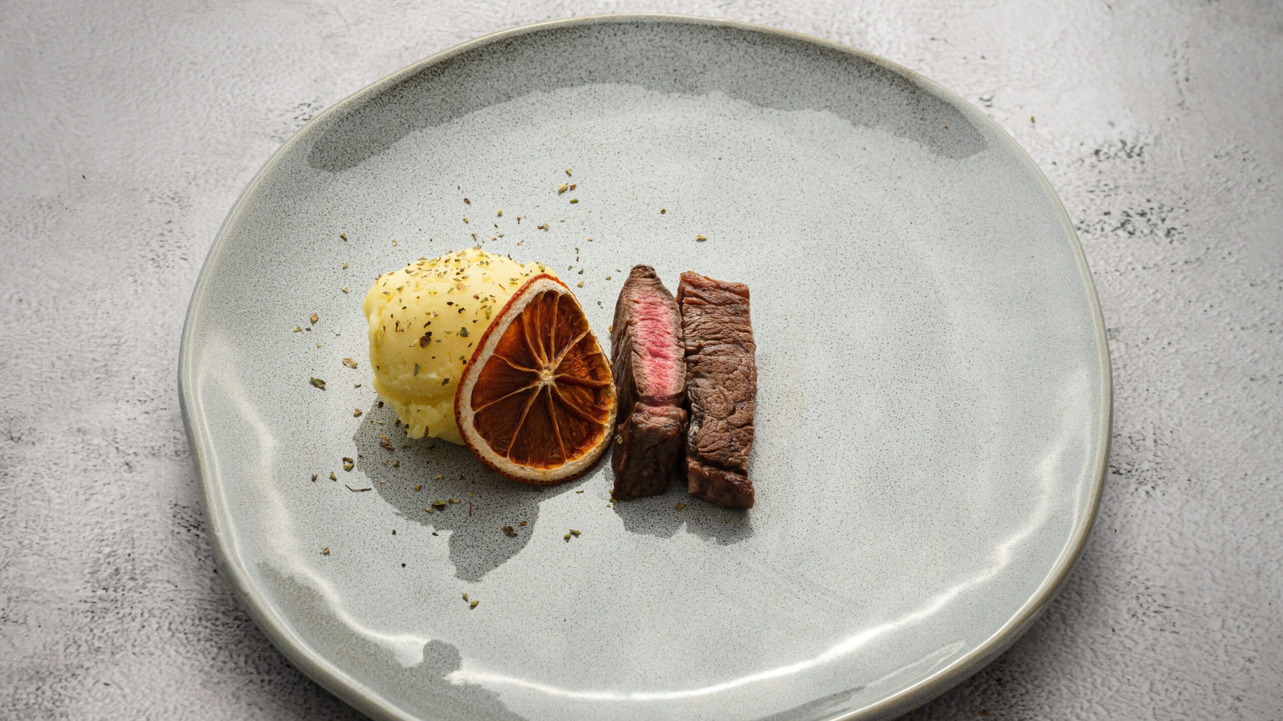 two tiny slices of steak with small scoop of mashed potato and a dried orange slice